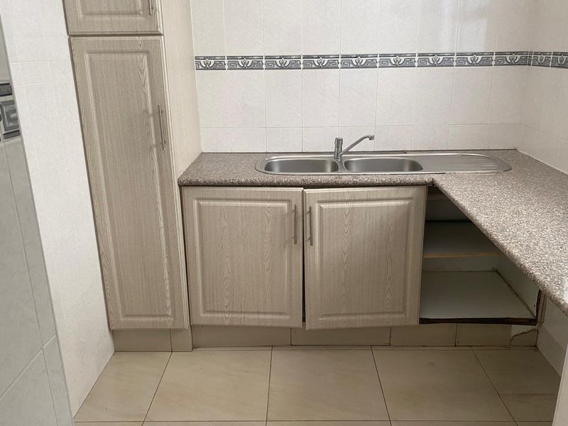 A functional kitchen area featuring light wood-grain cabinetry, a double stainless steel sink, and tiled splashbacks.