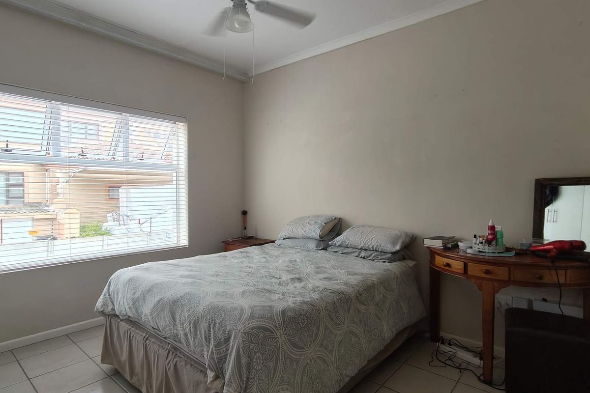 A functional bedroom featuring tiled flooring, a ceiling fan, and large windows with venetian blinds, offering a neutral canvas for potential updates.