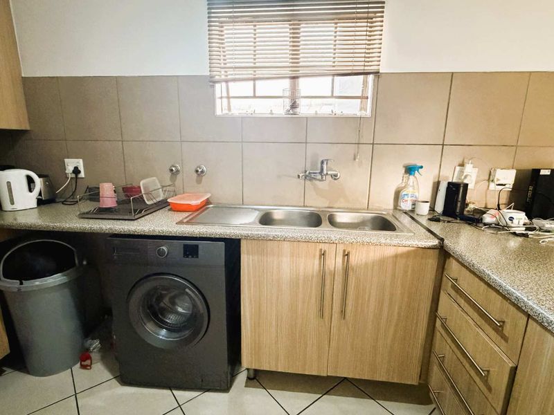 Functional kitchen area featuring laminate cabinetry, granite-look countertops, a double bowl stainless steel sink, and tiled splashbacks with integrated laundry plumbing.
