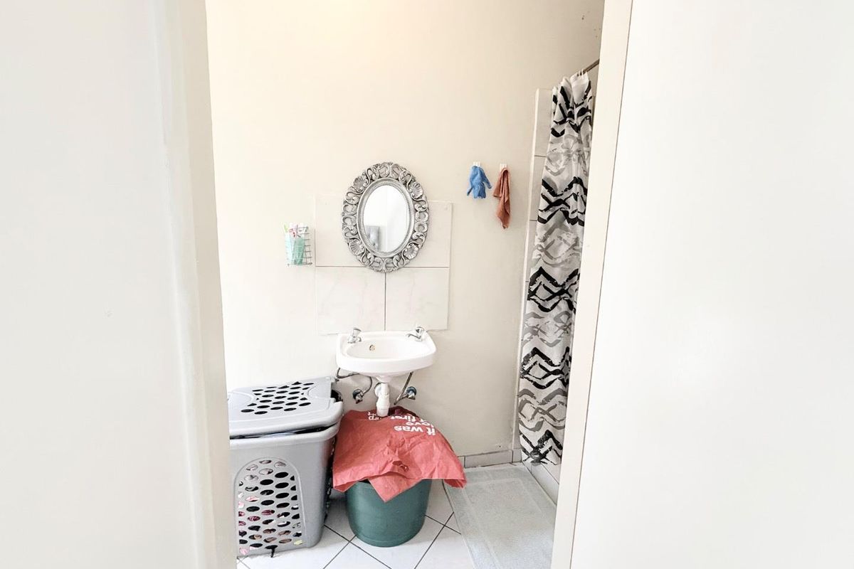 A compact bathroom featuring a wall-mounted basin, tiled flooring, and a shower cubicle with a curtain.