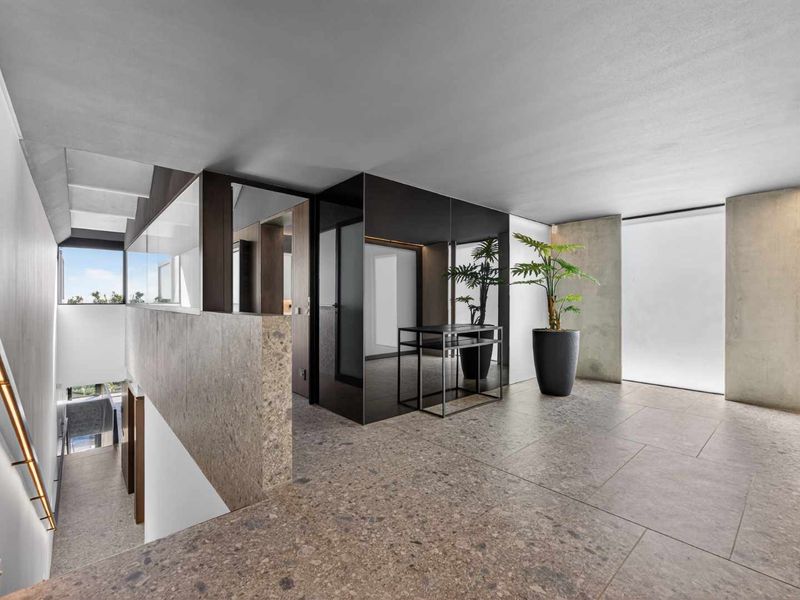 A modern, high-end hallway featuring premium stone tile flooring, architectural concrete walls, and a sleek staircase with integrated lighting.