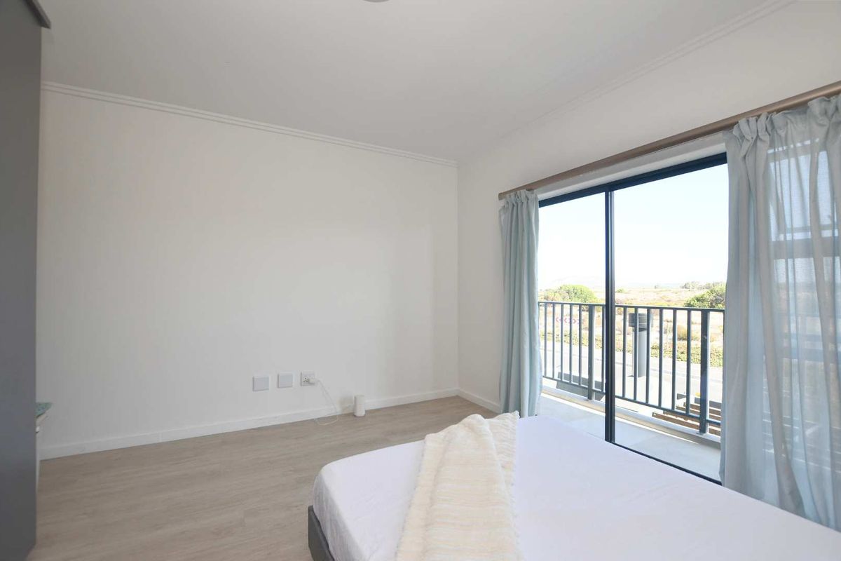 Bright bedroom featuring light laminate flooring and a sliding glass door that opens onto a private balcony with exterior views.