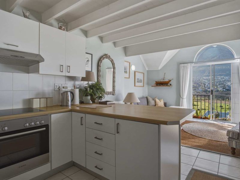 Open-plan kitchen and living area featuring white cabinetry, wooden countertops, exposed ceiling beams, and a sliding door leading to a balcony with scenic views.