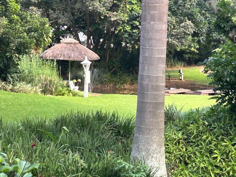 A lush, well-maintained garden featuring a small water feature, a thatched gazebo, and mature landscaping.