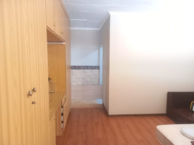 A bedroom featuring built-in wooden cupboards, laminate flooring, and neutral walls, with an adjacent tiled area visible through the doorway.