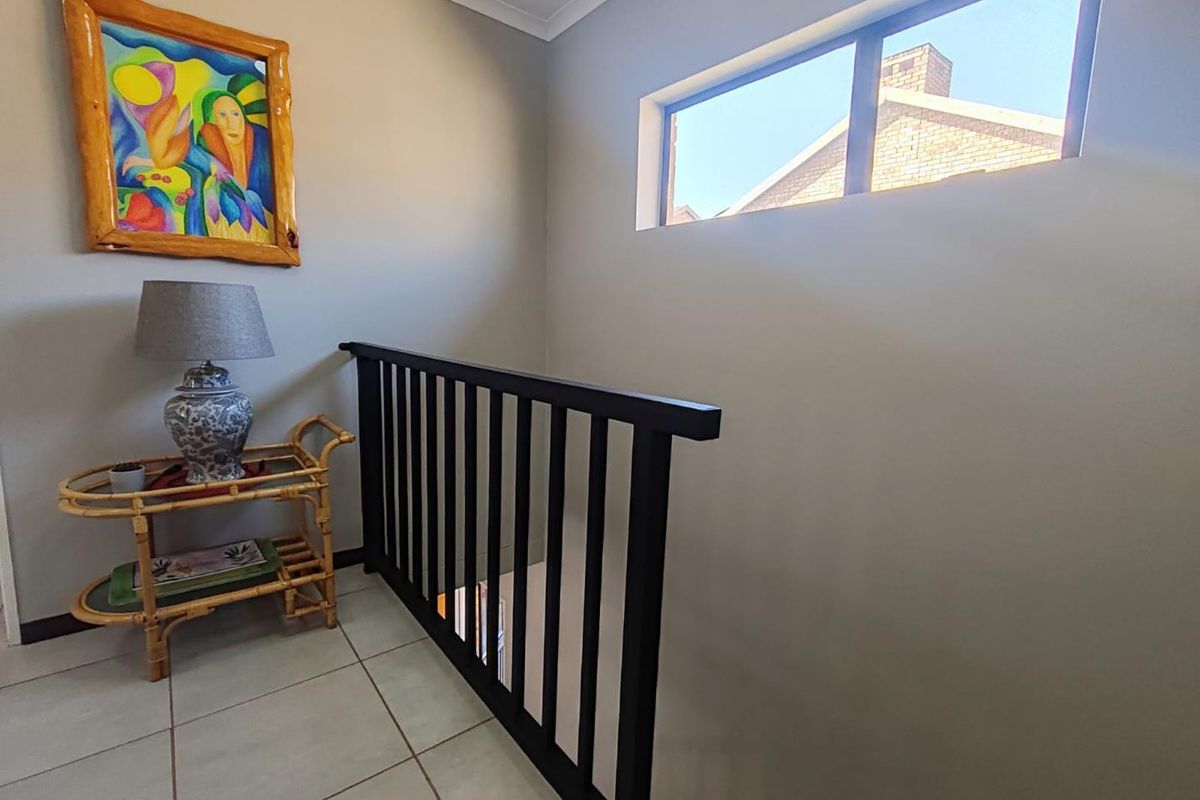 A bright landing area featuring a modern black balustrade, tiled flooring, and a high-set window providing natural light.