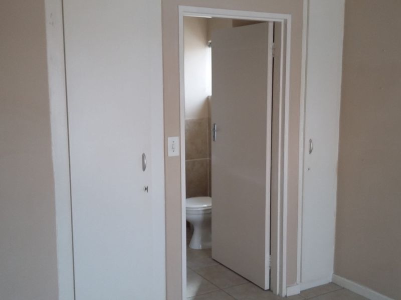 A clean, empty bedroom featuring built-in cupboards, tiled flooring, and a view into an adjoining bathroom.