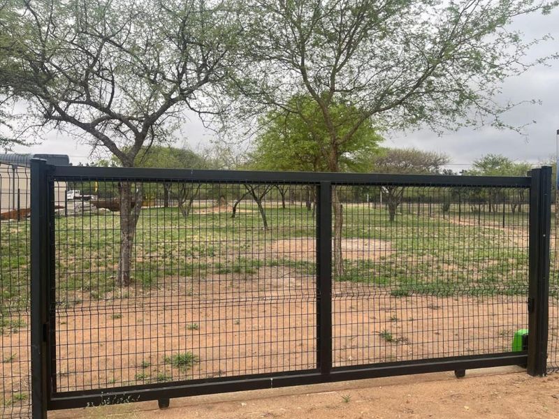 A view of the vacant commercial land secured by a modern black metal mesh gate and perimeter fencing.