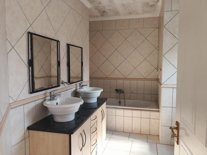 A dated bathroom featuring a double vanity with vessel sinks, a built-in bathtub, and tiled finishes, currently showing signs of ceiling water damage.