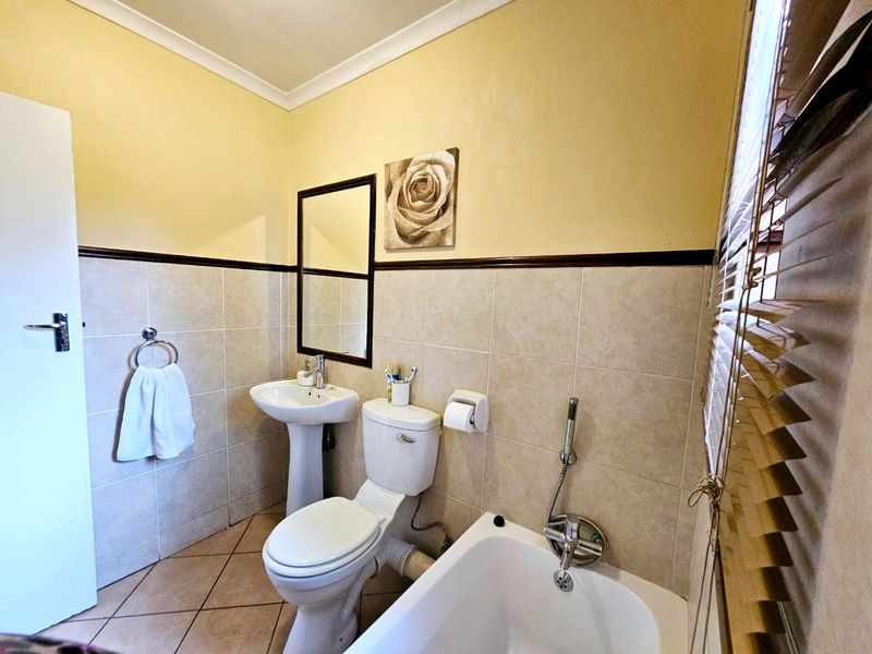 A functional bathroom featuring a pedestal washbasin, toilet, and bathtub with a handheld shower mixer, finished with neutral wall and floor tiles.
