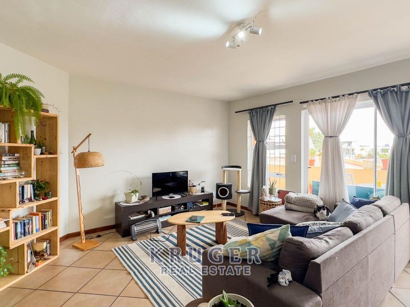 A comfortable living room featuring tiled flooring and a large sliding glass door that provides access to an outdoor balcony area.