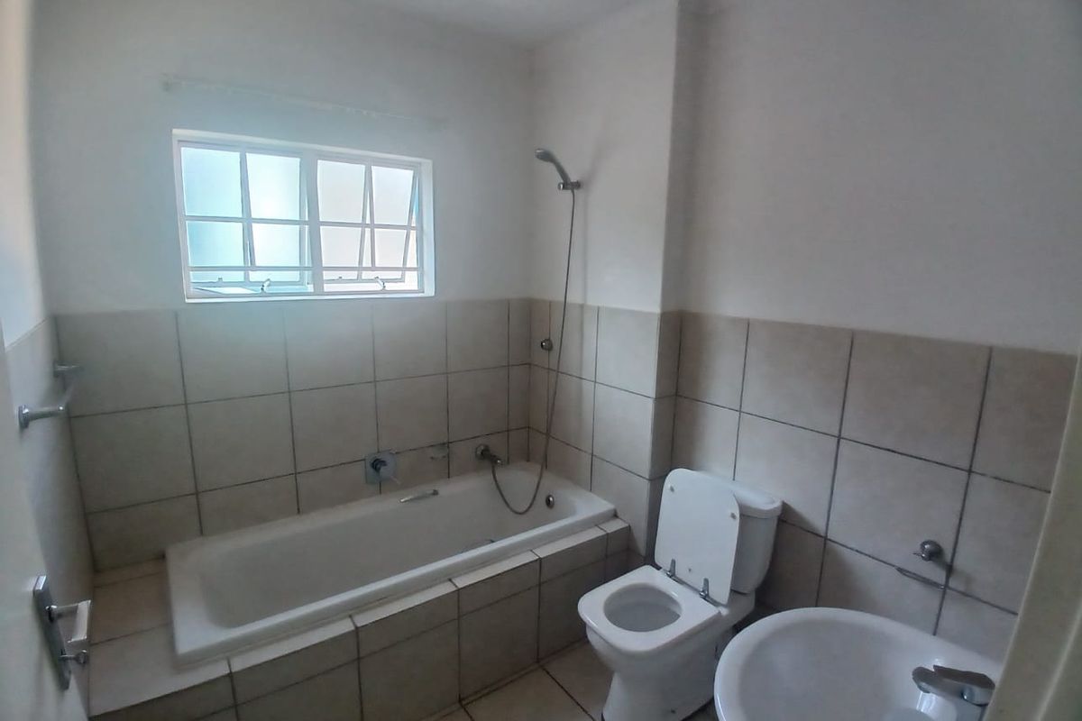 A functional bathroom featuring a built-in bathtub with shower attachment, a standard toilet, and a pedestal basin with neutral wall tiling.