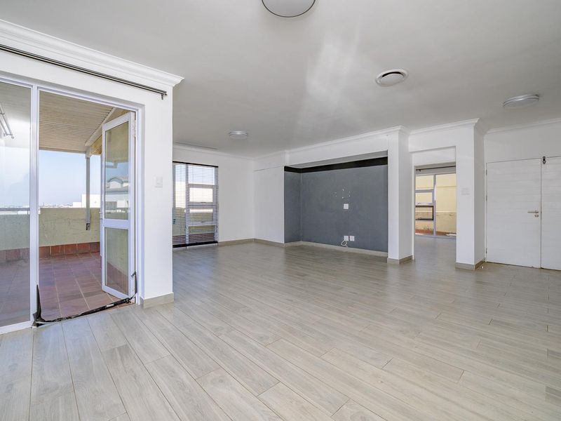Spacious open-plan living area featuring light wood-look laminate flooring, recessed lighting, and direct access to an outdoor balcony through sliding glass doors.
