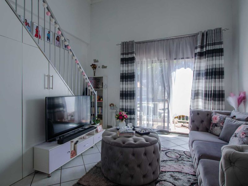 A bright living room featuring a staircase with built-in storage underneath, tiled flooring, and a sliding glass door providing access to the outdoor area.