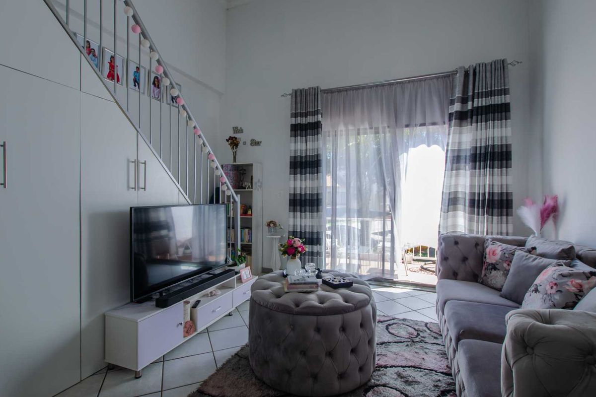 A bright living room featuring a staircase with built-in storage underneath, tiled flooring, and a sliding glass door providing access to the outdoor area.