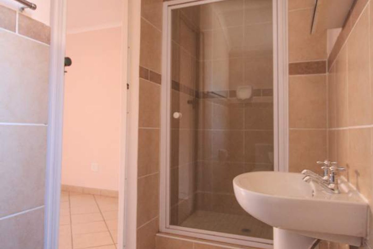 A functional bathroom featuring a pedestal basin, tiled walls and flooring, and a glass-enclosed shower unit.