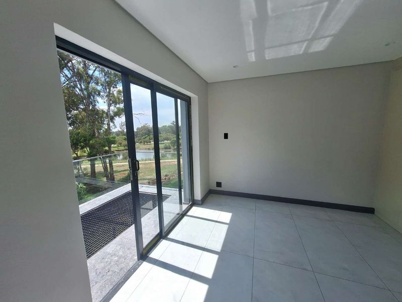 A bright, empty living area featuring large sliding glass doors that open onto a balcony with scenic views and modern tiled flooring.