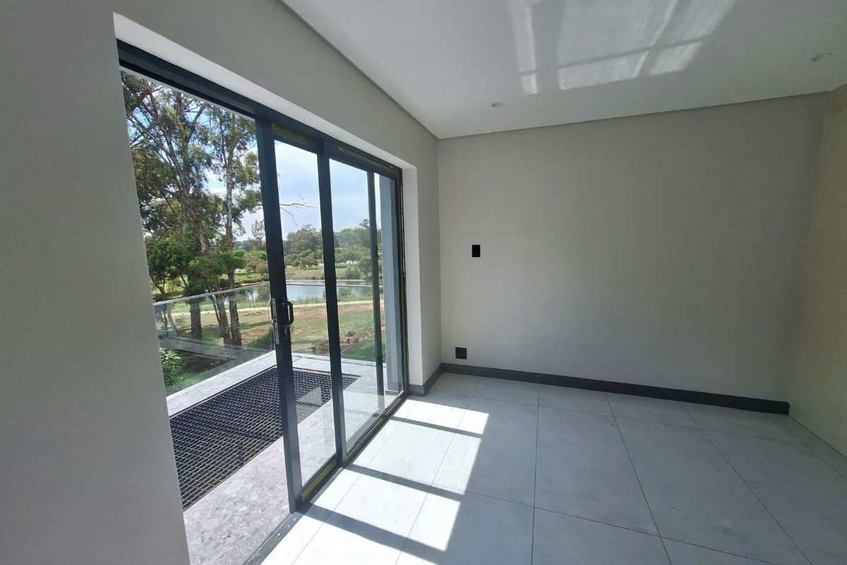 A bright, empty living area featuring large sliding glass doors that open onto a balcony with scenic views and modern tiled flooring.