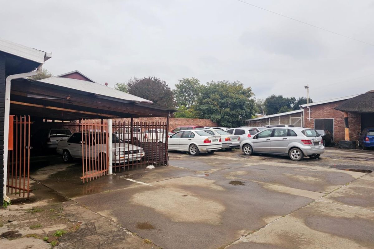 Exterior view of a commercial property featuring a paved parking area, covered parking bays, and perimeter brick walling.