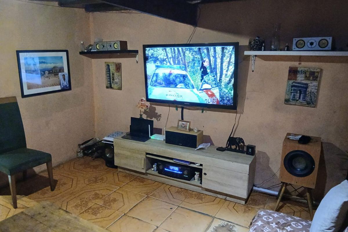 A living room featuring exposed ceiling beams and ceramic floor tiles, currently showing signs of wear and requiring cosmetic updates.