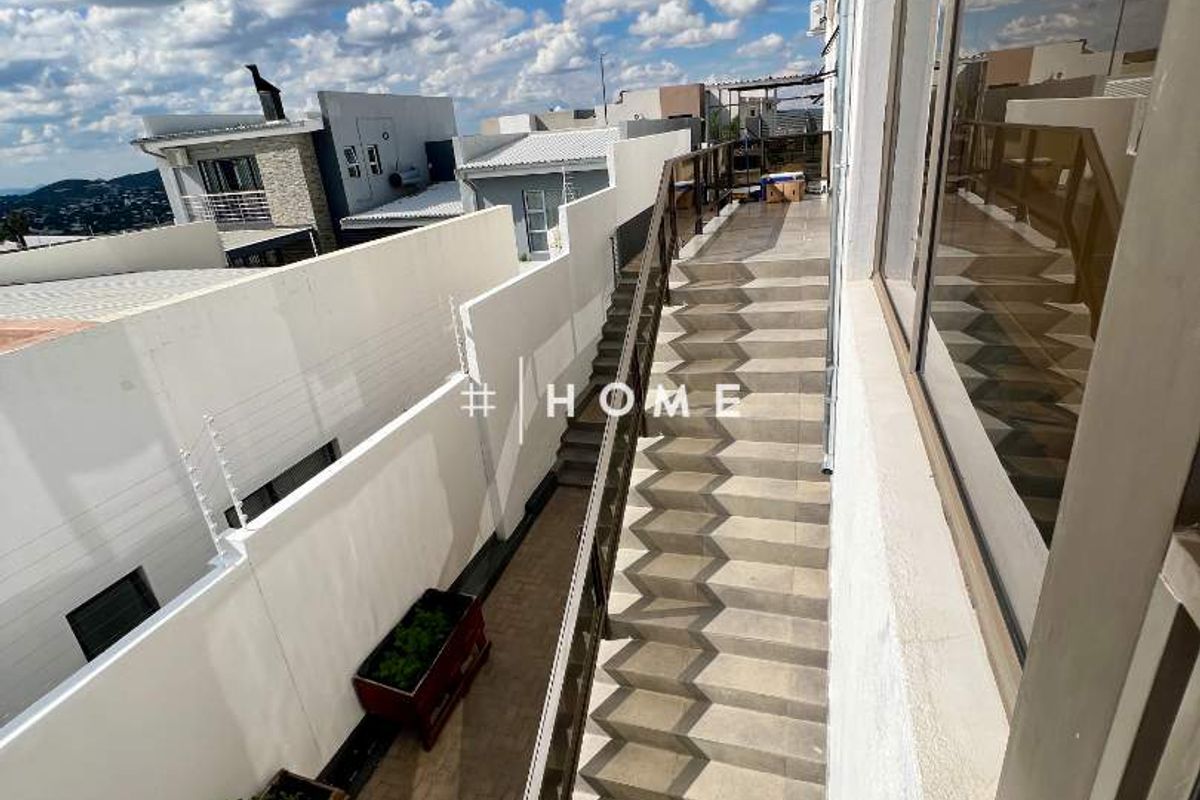An exterior view of a side walkway featuring a concrete staircase with metal railings, adjacent to a high boundary wall.