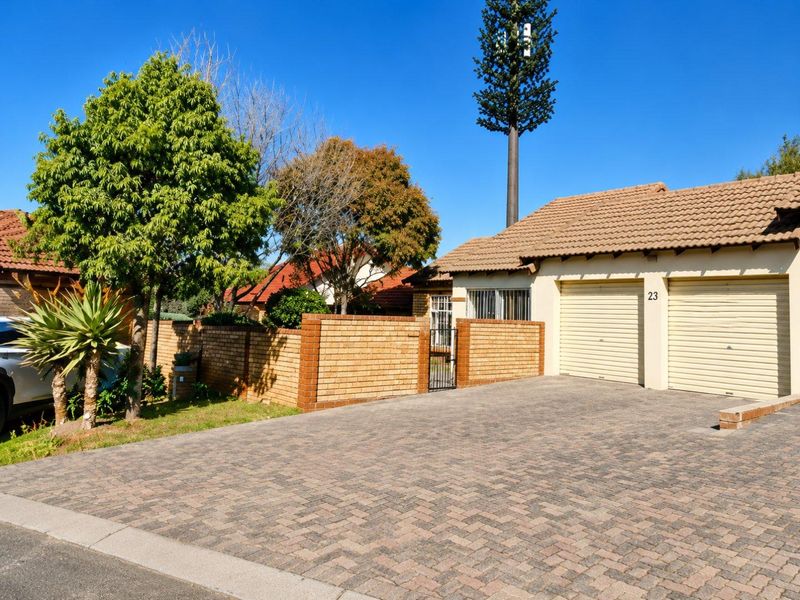Front view of the property featuring a paved driveway, double garage with roll-up doors, and a brick boundary wall with a security gate.