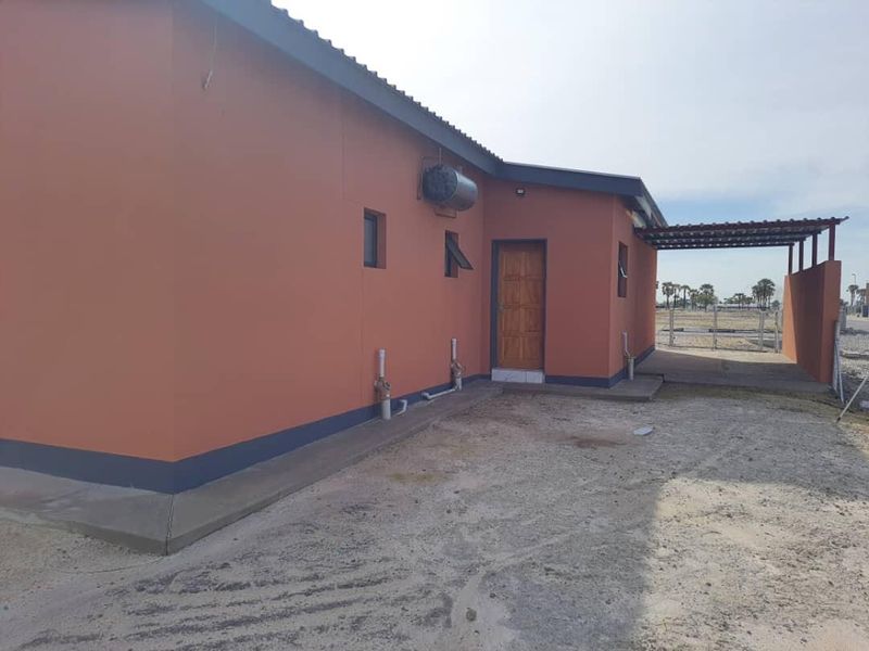 Rear view of the property featuring a covered patio area, external geyser, and unfinished ground surfaces.