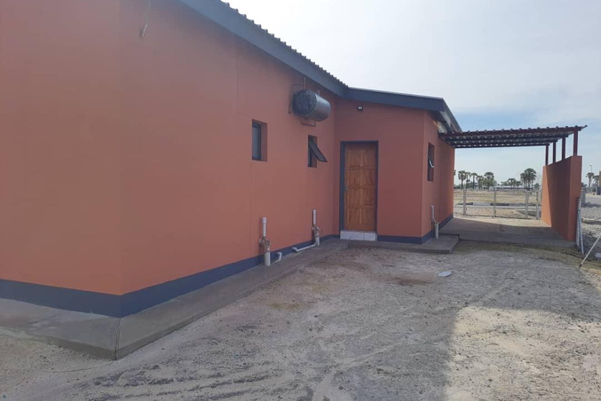 Rear view of the property featuring a covered patio area, external geyser, and unfinished ground surfaces.