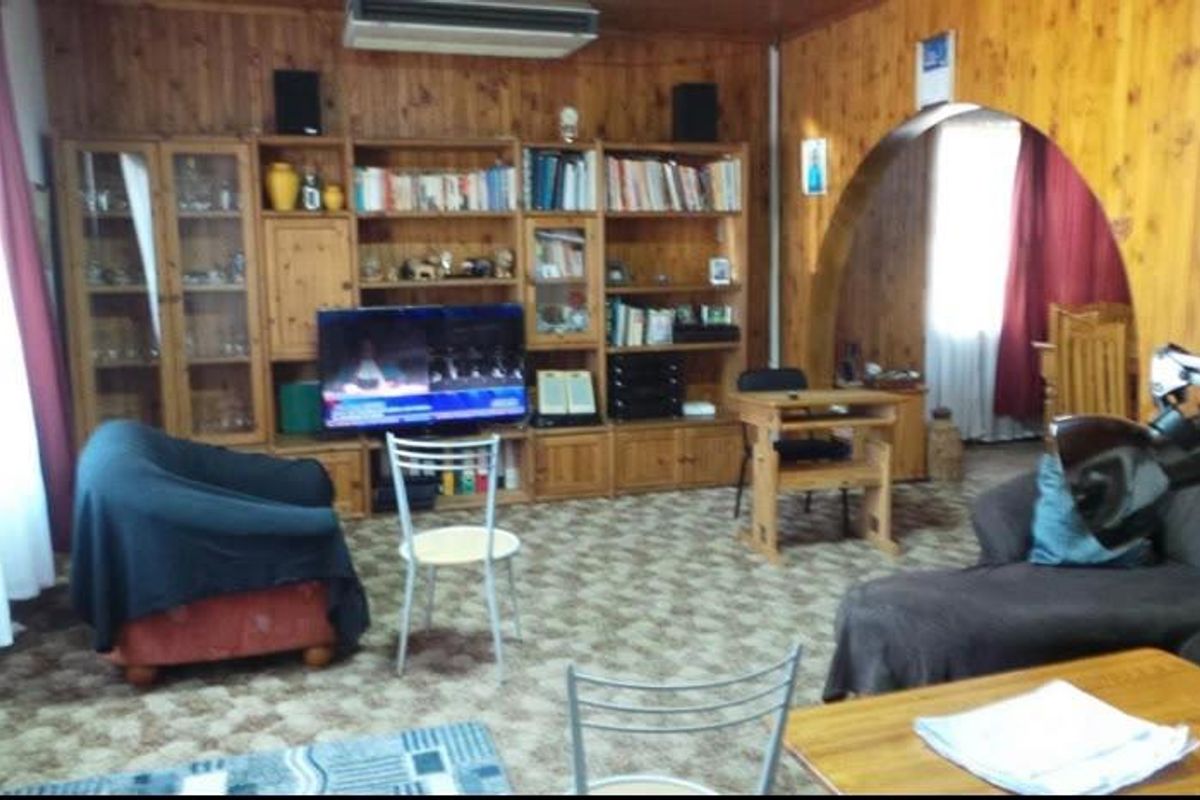 Living room featuring extensive wood paneling, a built-in wooden shelving unit, and an arched doorway leading to an adjacent space.