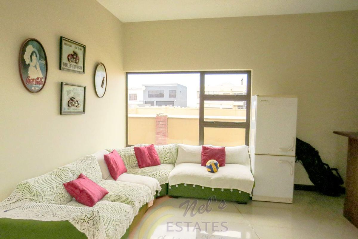 A living room area featuring large windows, tiled flooring, and neutral wall finishes, providing a bright and functional space.