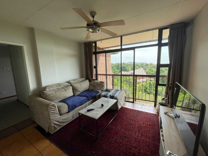 A living room featuring tiled flooring, a ceiling fan, and large sliding glass doors that open onto a balcony with scenic views.