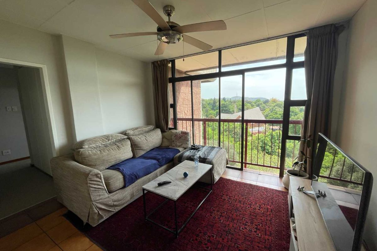 A living room featuring tiled flooring, a ceiling fan, and large sliding glass doors that open onto a balcony with scenic views.