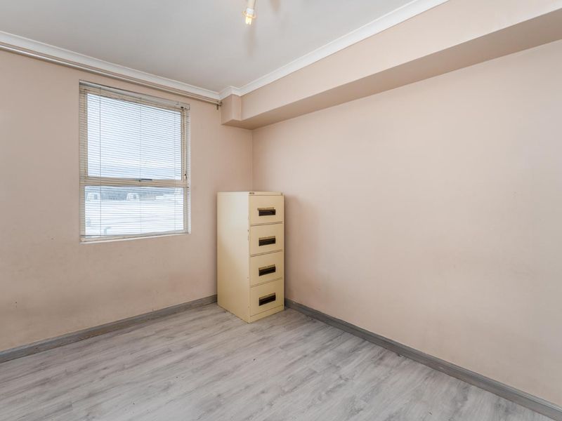 A vacant bedroom featuring light-toned walls, laminate flooring, and a window fitted with venetian blinds.