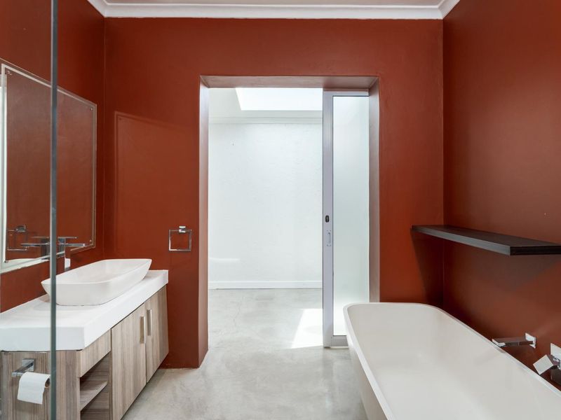 Modern bathroom featuring a vessel sink on a wood-finish vanity, a sleek freestanding bathtub, and a skylight providing natural light through a sliding door.
