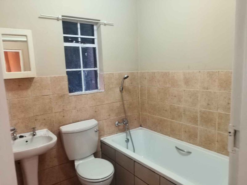 A functional bathroom featuring a pedestal basin, toilet, and a bathtub with a handheld shower mixer, finished with neutral wall tiling.