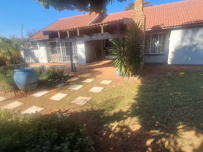 Rear view of the house featuring a covered brick patio, tiled roof, and a landscaped garden area with paved stepping stones.
