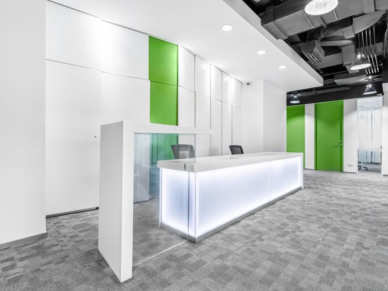 Modern office reception area featuring a sleek illuminated built-in desk, contemporary green accent walls, and an industrial-style exposed ceiling.