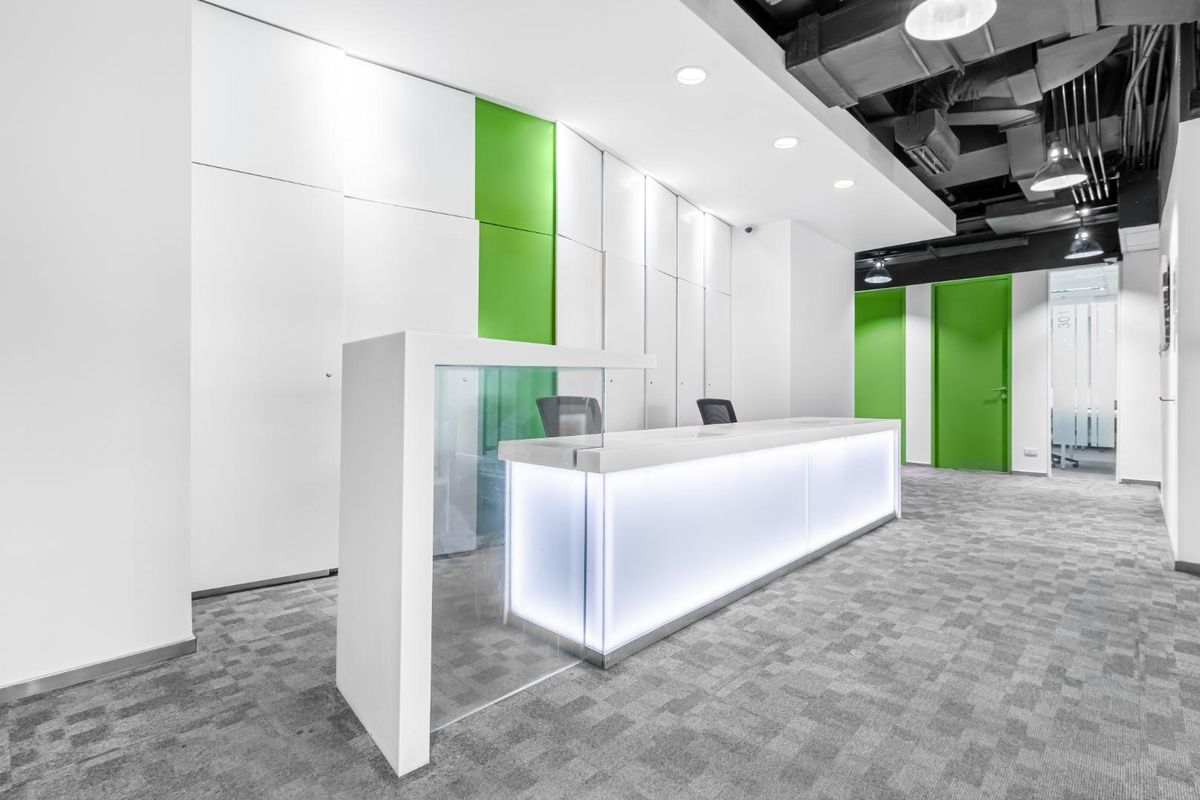 Modern office reception area featuring a sleek illuminated built-in desk, contemporary green accent walls, and an industrial-style exposed ceiling.