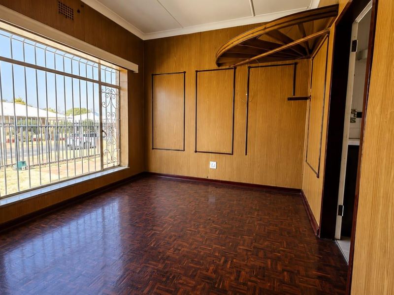 An empty living room featuring dated wood paneling, parquet flooring, and large windows with security bars.