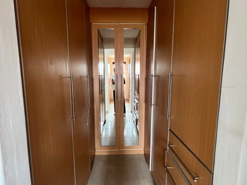 A functional walk-through dressing area or hallway featuring extensive built-in wooden cabinetry with integrated mirrored doors and tiled flooring.
