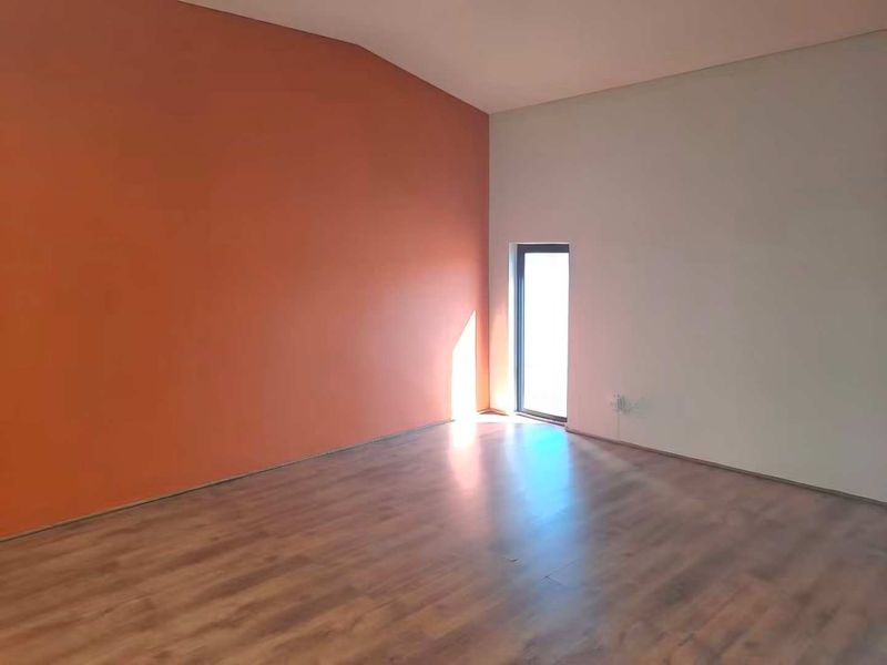 An empty living room featuring laminate flooring and a dual-tone wall finish with a single window providing natural light.