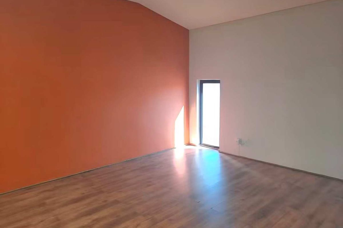 An empty living room featuring laminate flooring and a dual-tone wall finish with a single window providing natural light.