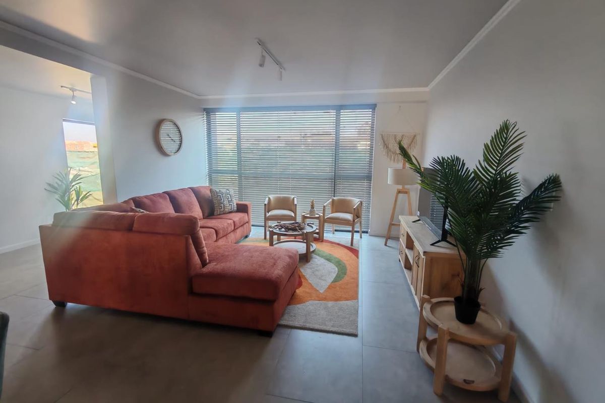 A bright and spacious living room featuring large windows with venetian blinds and neutral tiled flooring, offering a comfortable and well-lit living area.