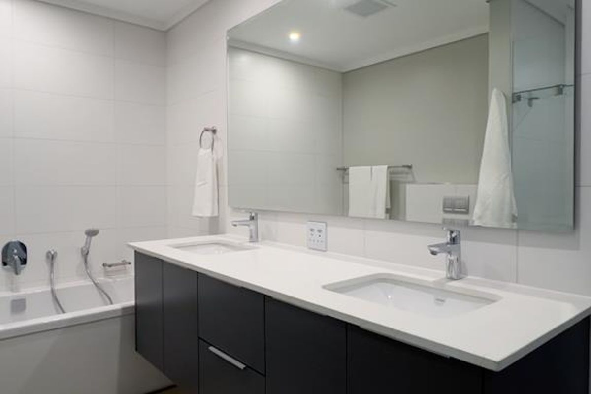 Modern bathroom featuring a sleek double vanity with undermount sinks, a large wall mirror, and a built-in bathtub with contemporary tiled finishes.