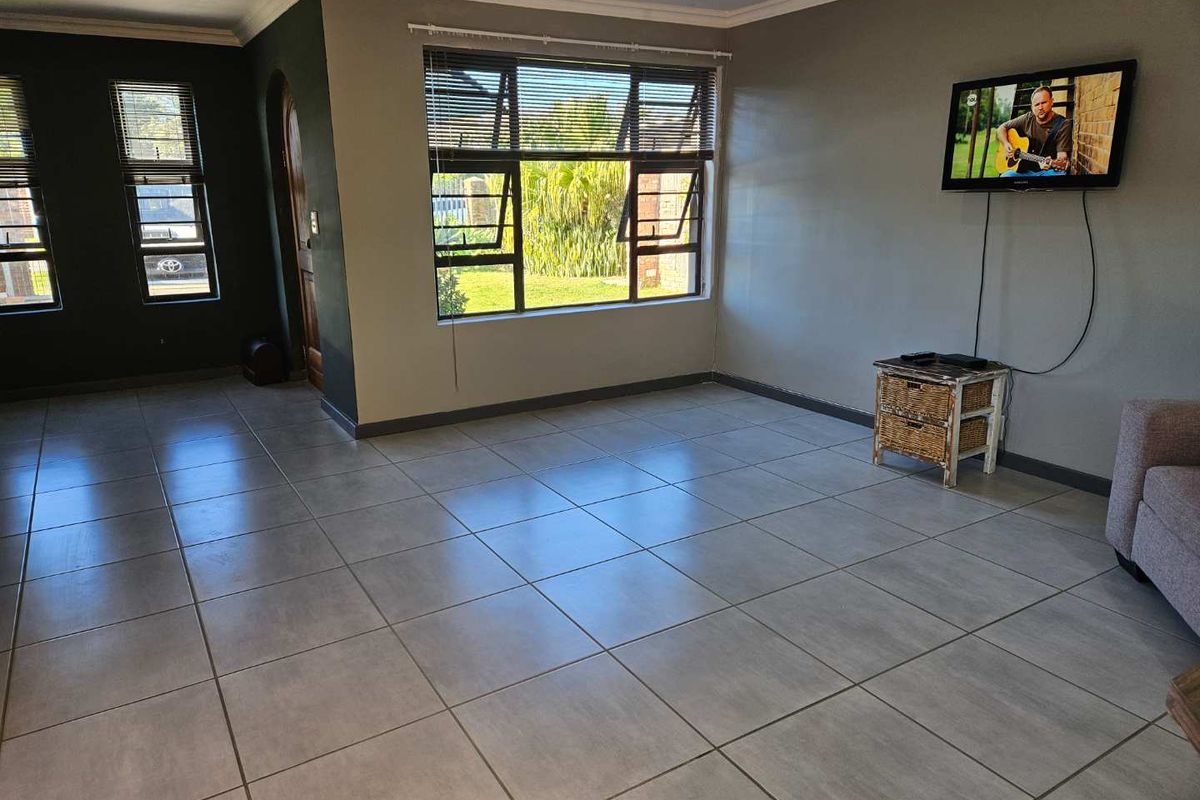 A spacious living room featuring neutral tiled flooring, large aluminium-framed windows, and a classic archway leading to the entrance.