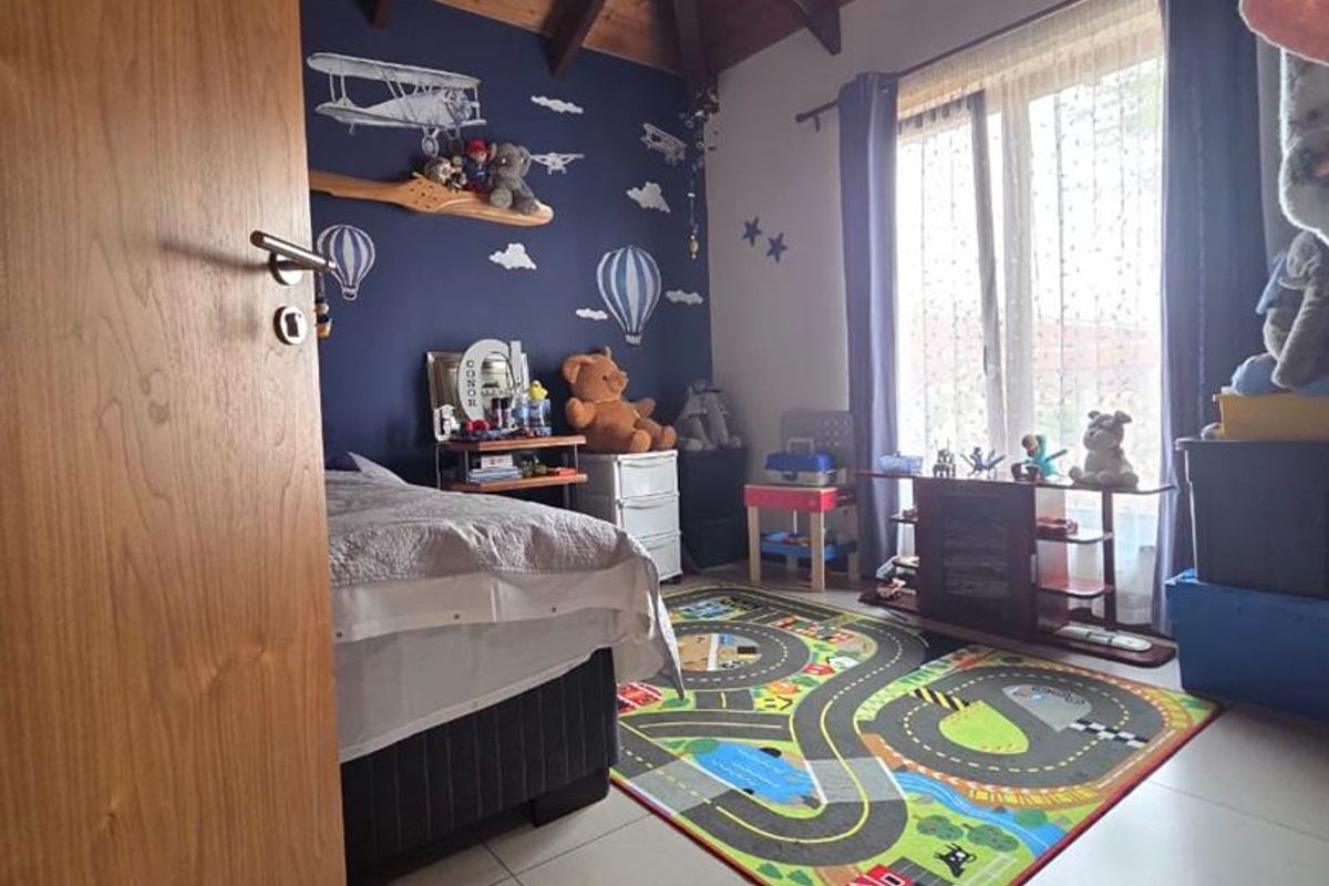 A bedroom featuring a vaulted timber-beamed ceiling, tiled flooring, and a large window providing natural light.