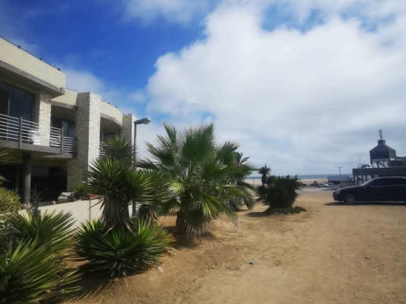 Exterior view of the property facade featuring stone cladding and balcony access, situated on an unpaved lot near the coast.