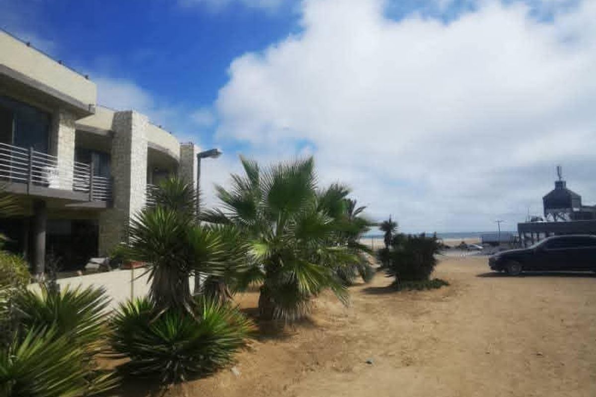 Exterior view of the property facade featuring stone cladding and balcony access, situated on an unpaved lot near the coast.
