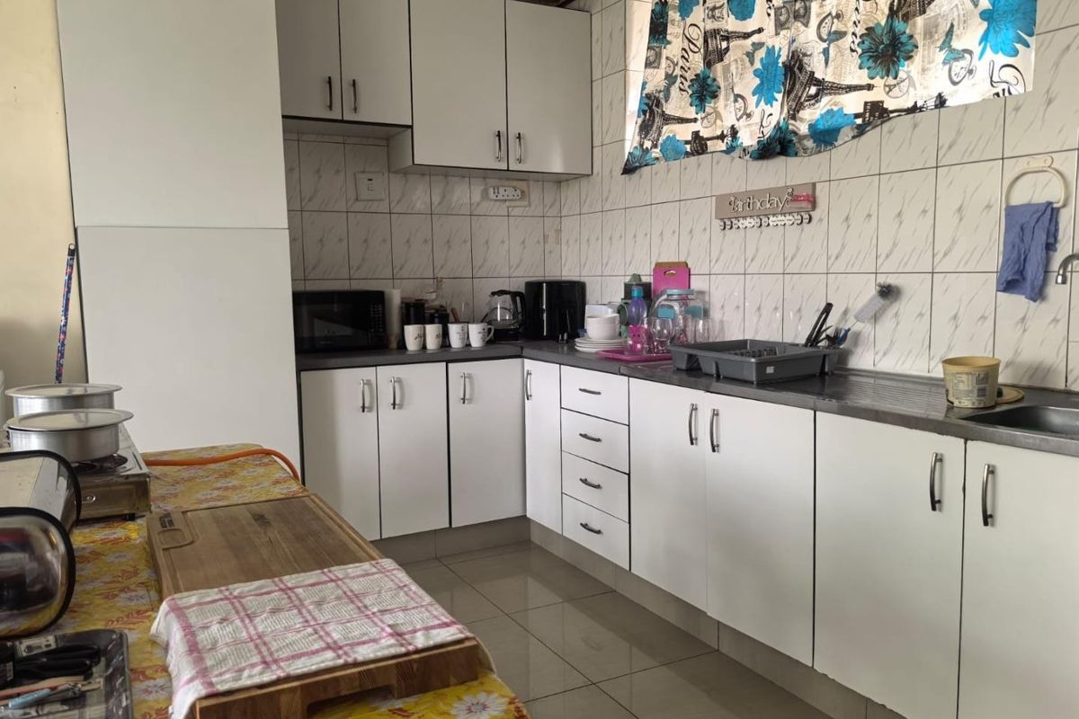 A functional kitchen featuring white built-in cabinetry, tiled backsplash, and tiled flooring, offering a practical layout for daily meal preparation.