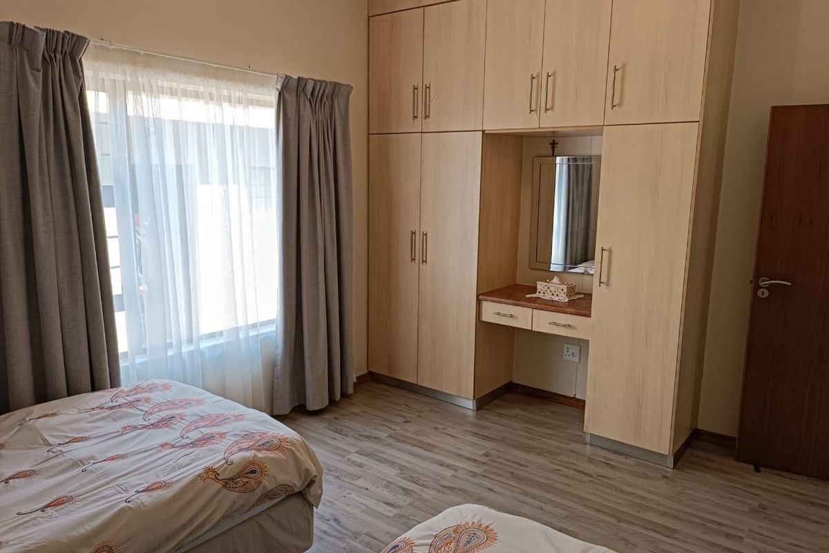 A well-maintained bedroom featuring light wood-finish built-in cupboards with an integrated vanity area and durable laminate flooring.